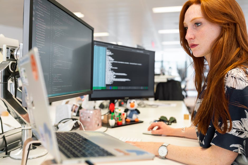 A focused female software engineer coding on dual monitors